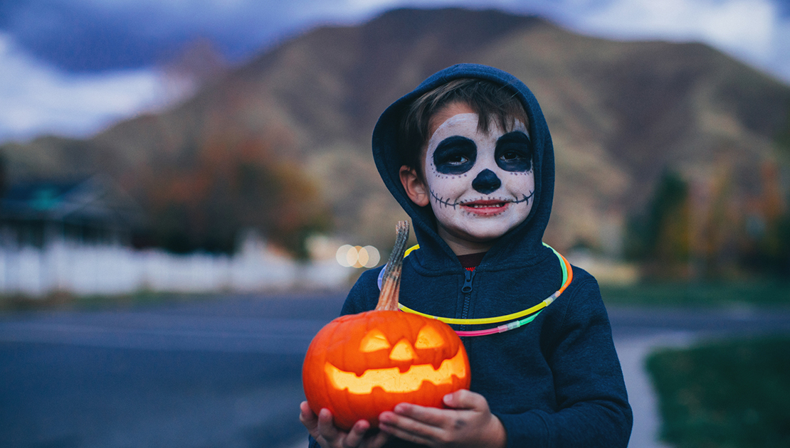 child dressed in costume, holding a pumpkin, wearing a set of glowsticks for visibility