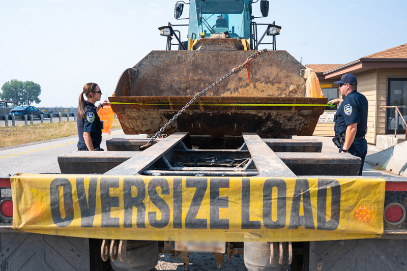Two people in MCS law enforcement clothing looking at an oversized load