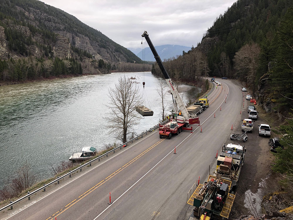 A crane lifts construction material alongside Flathead River Image