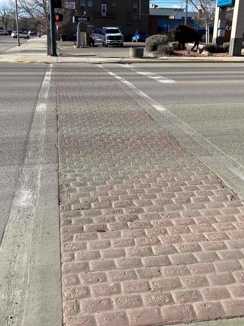 Photo showing decorative stamped concrete crosswalk with a brick-pattern surface and white painted crosswalk striping, which MDT will replace as part of the project.