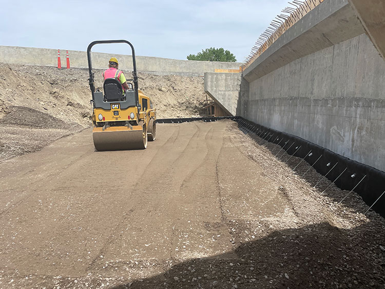 Riverside Construction is backfilling and compacting the soil behind the bridge’s concrete backwall to provide additional stabilization.