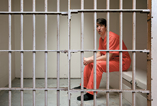 person wearing orange jump suit behind bars
